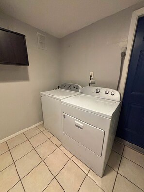 A laundry room with two stacked washers and dryers, a tiled floor, and a blue door. - Spacious 4BR Home • 2 Kitchens • Sleeps 8 (Houston)