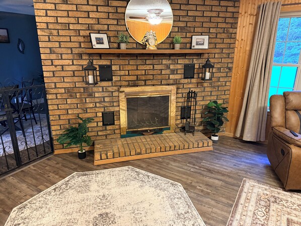A brick fireplace with a mantel, surrounded by potted plants, and a large mirror above it. -  Wooded 3BR • Kayaks & RV Parking • 3 Mi to Brady Mtn Marina (Royal)