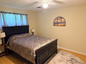 Une chambre à coucher comprenant un lit, une table de chevet, une lampe, un ventilateur de plafond et un tableau accroché au mur.