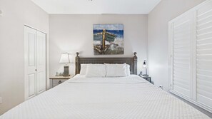 A bedroom with a large bed, a nightstand with a lamp, a painting on the wall, and a door. - Seas the View 2008-Beach Resort-Sleeps 6 (Panama City)