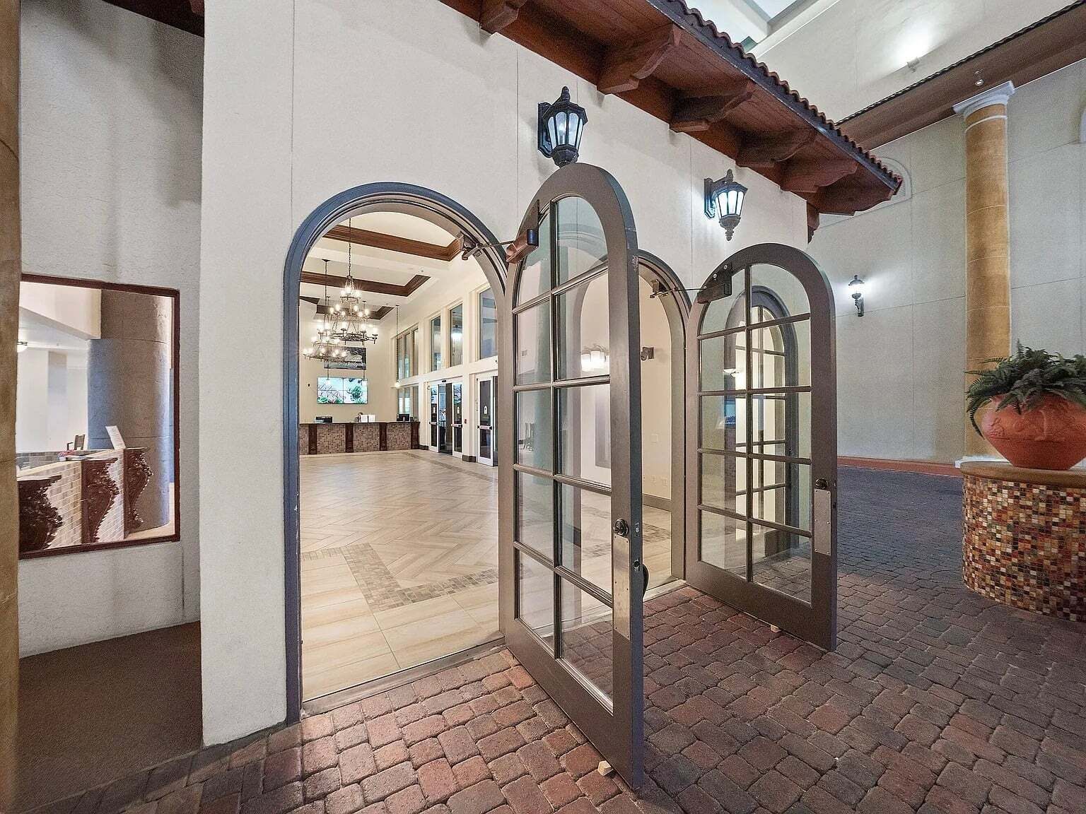 A spacious lobby with arched doorways, a tiled floor, and a large potted plant.