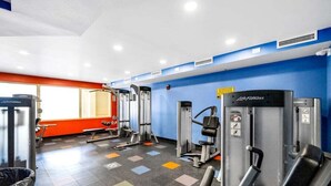 Et fitnesscenter med forskellige træningsmaskiner, en rød væg og et vindue.