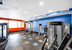 Ein Fitnessraum mit verschiedenen Trainingsgeräten, einer roten Wand und einem Fenster.