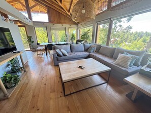 Un vaste espace de vie doté d’un plancher en bois, d’un canapé gris, d’une table basse et d’un téléviseur posé sur un meuble en bois.