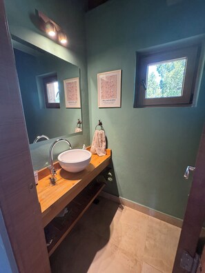 Un baño con tocador de madera, un espejo grande, un lavamanos y cuadros en la pared.