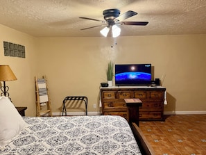A bedroom with a bed, a dresser, a ceiling fan, a television displaying a space scene, and a window with blinds. - Charming Southwest Hacienda 4Br/4.5Ba (Anthony)