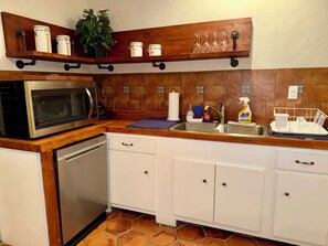 A kitchen with a microwave, dishwasher, white cabinets, a wooden countertop, and a shelf with jars and glasses. - Charming Southwest Hacienda 4Br/4.5Ba (Anthony)