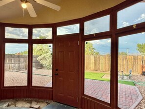 A room with a large windowed door, a ceiling fan, and a view of a backyard with a wooden fence and greenery. - Charming Southwest Hacienda 4Br/4.5Ba (Anthony)