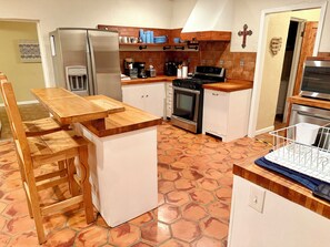 A compact kitchen with a central island, a refrigerator, stove, and a microwave. - Charming Southwest Hacienda 4Br/4.5Ba (Anthony)