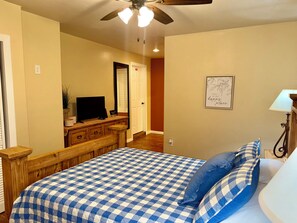 A bedroom with a checkered bedspread, a television on a wooden dresser, a ceiling fan, and a framed quote on the wall. - Charming Southwest Hacienda 4Br/4.5Ba (Anthony)