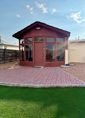 A wooden gazebo with a red door and large windows, surrounded by a brick patio and a green lawn. - Charming Southwest Hacienda 4Br/4.5Ba (Anthony)