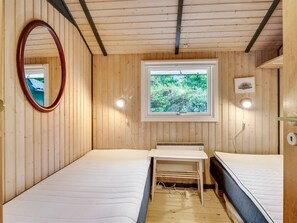 Ein kleiner, gemütlicher Raum mit Holzwänden und einem Fenster. Es gibt zwei Betten, einen Spiegel und einen kleinen Tisch mit einem Heizgerät.