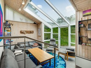 Ein modernes Interieur mit Glasdecke, grauen Sofas, einem Holztisch und einem blau gemusterten Teppich.