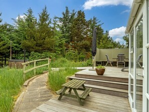 A wooden deck with a picnic table and chairs, surrounded by lush greenery and trees.