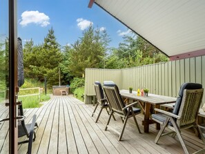 Une terrasse en bois avec un jacuzzi, des sièges d’extérieur et une vue sur la verdure environnante.