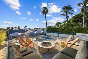 A rooftop lounge area with lounge chairs, a fire pit, and a view of palm trees and the sky. - Stay SanDi - Resort Style Paradise | Pool Hot Tub, Renovated, AC (San Diego)