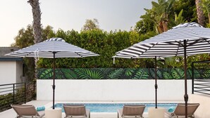 Ein Poolbereich mit Liegestühlen, gestreiften Sonnenschirmen und einem Tisch mit einer Flasche und Gläsern.