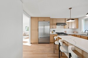 A modern kitchen with a stainless steel refrigerator, wooden cabinets, a marble countertop, and bar stools. - Stay SanDi - Resort Style Paradise | Pool Hot Tub, Renovated, AC (San Diego)