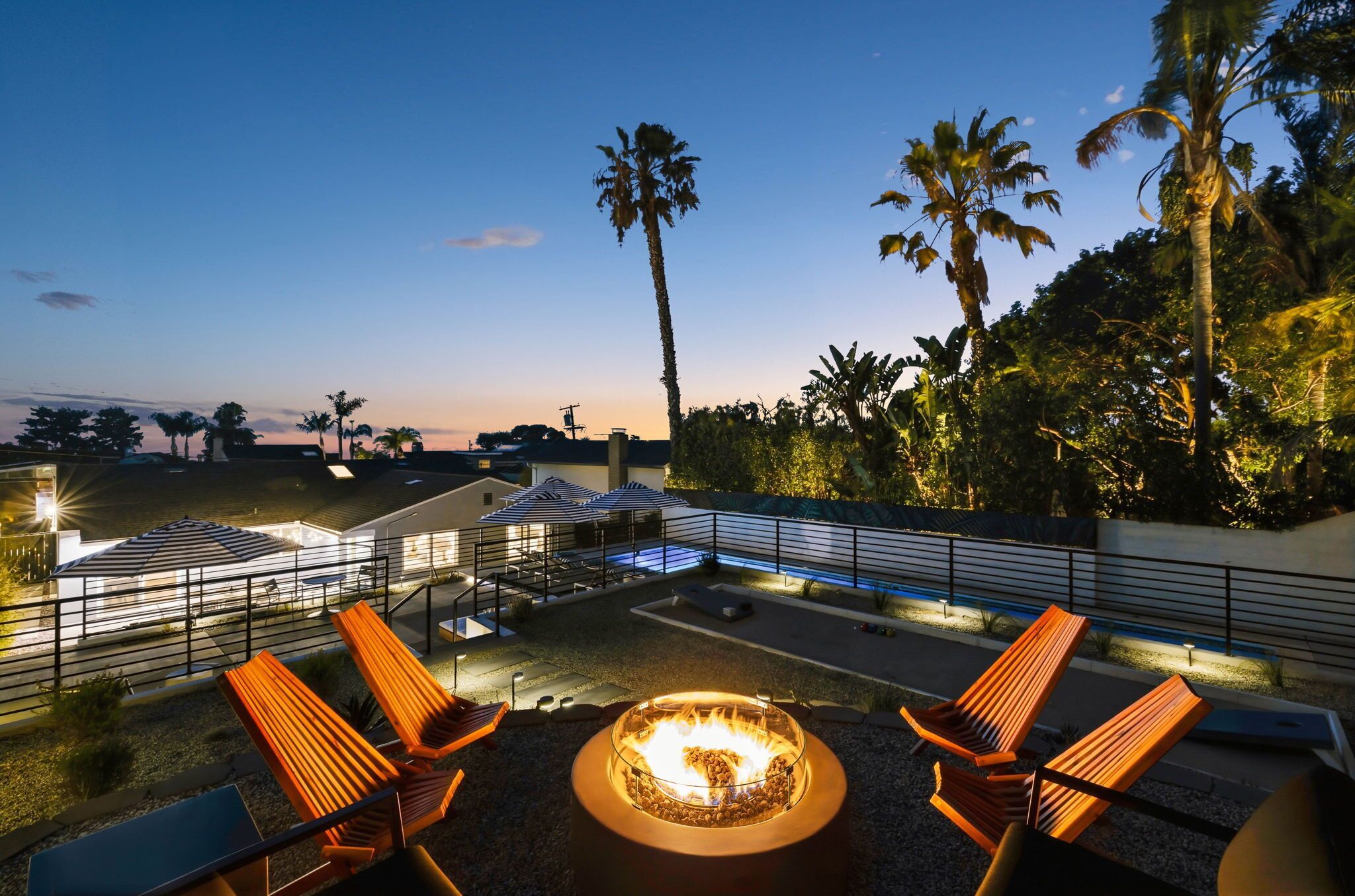 Un espace extérieur aménagé avec des fauteuils confortables et un foyer, entouré de palmiers et offrant une vue sur le coucher du soleil.