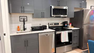 A modern kitchen with grey cabinets, a stainless steel microwave, oven, and dishwasher, and a blue chair.