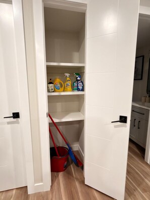 Een witte kast met planken, gevuld met schoonmaakspullen en een dweil.