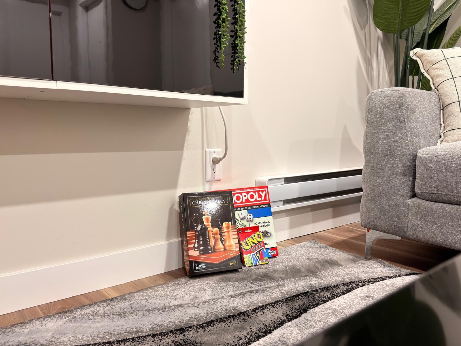 Una sala de estar con un sofá gris, un juego de ajedrez y un televisor montado en la pared.