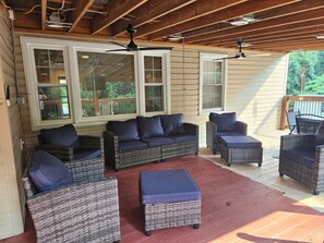 Une terrasse extérieure aménagée avec des meubles en osier, notamment un canapé et un pouf, ainsi qu’un ventilateur de plafond.