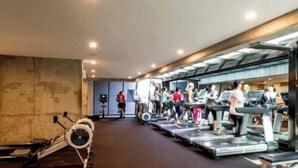 Academia com esteiras e bicicletas ergométricas, um espelho grande e uma parede com design texturizado.