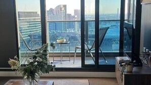 Uma sala de estar moderna com uma grande porta de vidro deslizante que dá para uma varanda com vista para a cidade.