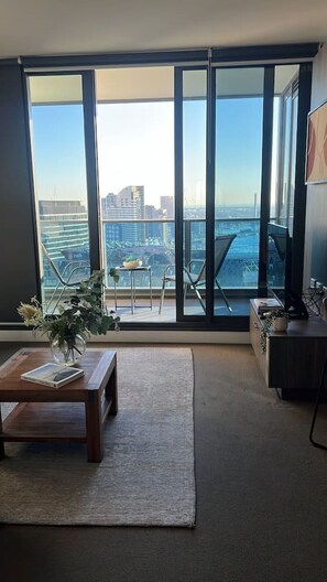 Ein modernes Wohnzimmer mit einem großen Schiebeglasfenster, das auf einen Balkon mit Blick auf die Stadt führt.