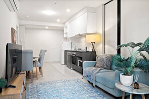 A modern living room with a sofa, a coffee table, a TV, and a kitchen area with cabinets and appliances. - Collins St CBD escape| Pool, Gym, Sauna & Parking (Melbourne)