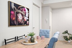 A dining area with a wooden table, chairs, a painting, and a potted plant. - Collins St CBD escape| Pool, Gym, Sauna & Parking (Melbourne)