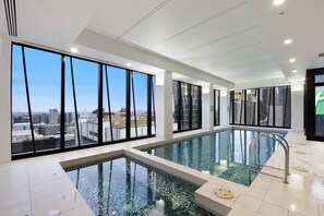 A modern indoor pool with large windows offering city views. - Collins St CBD escape| Pool, Gym, Sauna & Parking (Melbourne)