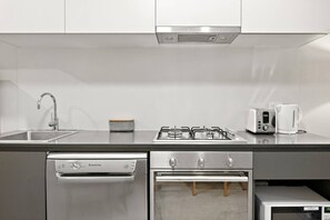 A modern kitchen with a stainless steel sink, a gas stove, a built-in oven, and a coffee maker. - Collins St CBD escape| Pool, Gym, Sauna & Parking (Melbourne)