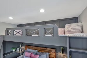 A bunk bed with a wooden headboard, a bedside table with a plant, and a wall-mounted lamp. - The Swiftie: Sleeps 5, Pool, City & River Views, Near Broadway (Nashville)