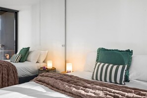 Ein Hotelzimmer mit einem Bett, zwei Nachttischen mit Lampen, einem großen Spiegel und Blick ins Freie.
