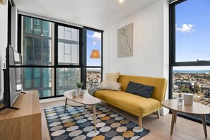 Ein modernes Wohnzimmer mit einem gelben Sofa, einem Couchtisch und Blick auf die Stadt durch große Fenster.