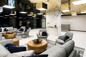 Eine moderne Lobby mit grauen Sofas, runden Couchtischen und einem Marmor-Empfangsschalter.