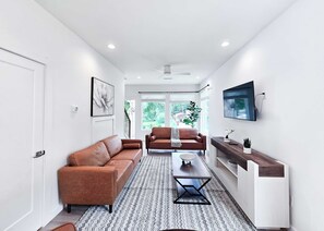 Ein modernes Wohnzimmer mit einem braunen Ledersofa, einem Couchtisch und einem an der Wand befestigten Fernseher.