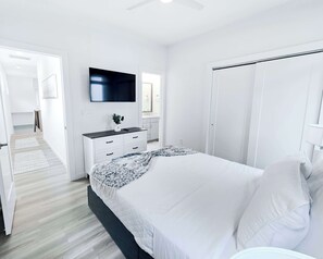A bedroom with a bed, a TV, a wardrobe, and a bathroom visible through an open door. - Balcony | 5 Min to Duke + Downtown (Durham)