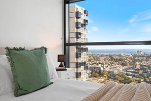 A bedroom with a large window, a bed, a nightstand with a lamp, and a view of a cityscape. - Tiara Southbank 2BR Pool & Parking. Walk to Crown (Southbank)