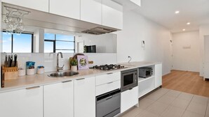 Cozinha moderna com armários brancos, eletrodomésticos de aço inoxidável e uma grande janela que oferece iluminação natural.