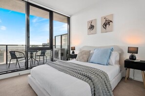 A bedroom with a large bed, two bedside lamps, a view of the city through floor-to-ceiling windows, and a balcony with chairs. - Tiara Southbank 2BR Pool & Parking. Walk to Crown (Southbank)