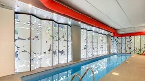 Uma piscina interior com parede de vidro, teto vermelho e chão revestido com azulejos.