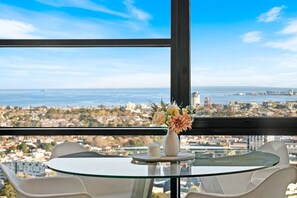 A glass table with a vase of flowers, white chairs, and a view of a coastal cityscape. - Tiara Southbank 2BR Pool & Parking. Walk to Crown (Southbank)