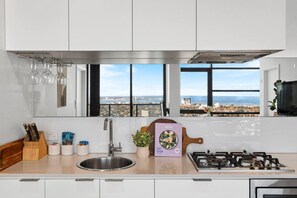 A modern kitchen with a stainless steel sink, a gas stove, and a window offering a city view. - Tiara Southbank 2BR Pool & Parking. Walk to Crown (Southbank)