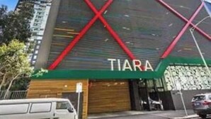 Um edifício moderno com uma placa grande 'TIARA' na fachada, rodeado por árvores e outros edifícios.