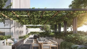 Uma área moderna para refeições ao ar livre, com uma mesa comprida e cadeiras, rodeada por vegetação exuberante e um elemento aquático.