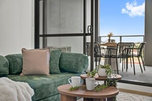 Ein Balkon mit einer grünen Couch, einem kleinen runden Tisch mit einer weißen Tasse und einem Topf mit einer Pflanze.