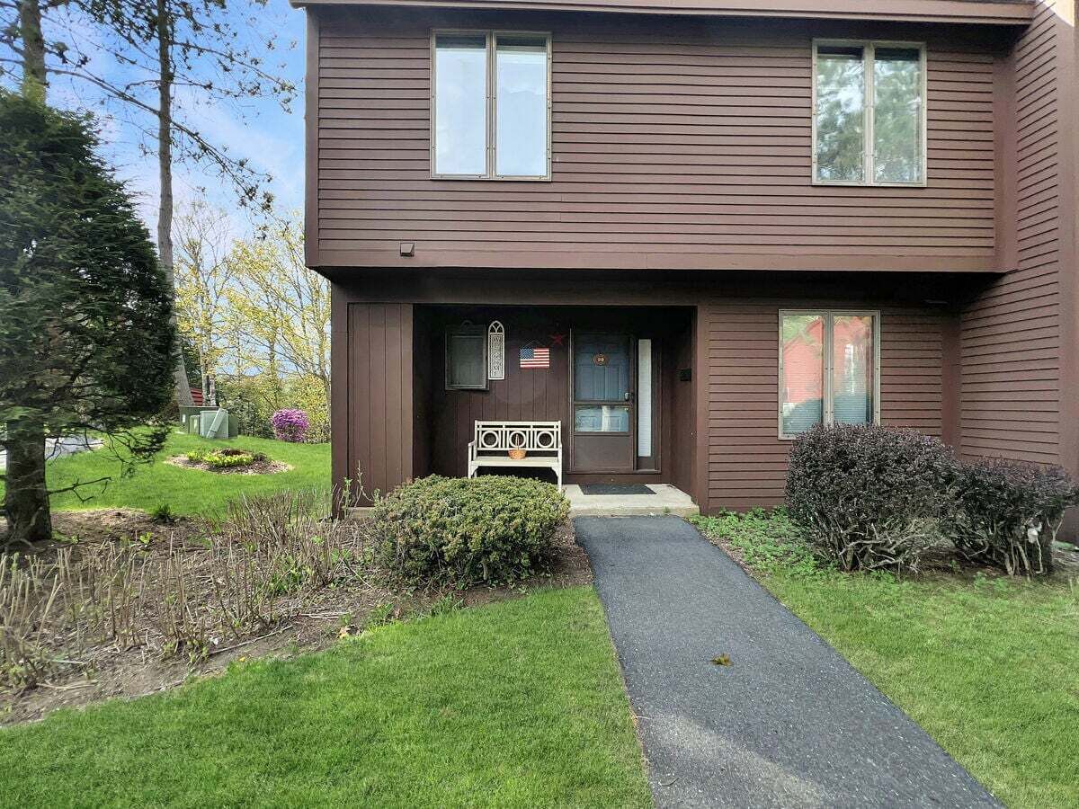 A two-story residential building with a front porch, a mailbox, and a small garden area.